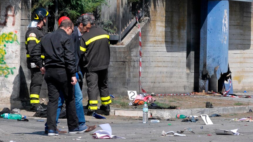 Italian policemen and firefighters inspect the site where a bomb exploded in front of a school.