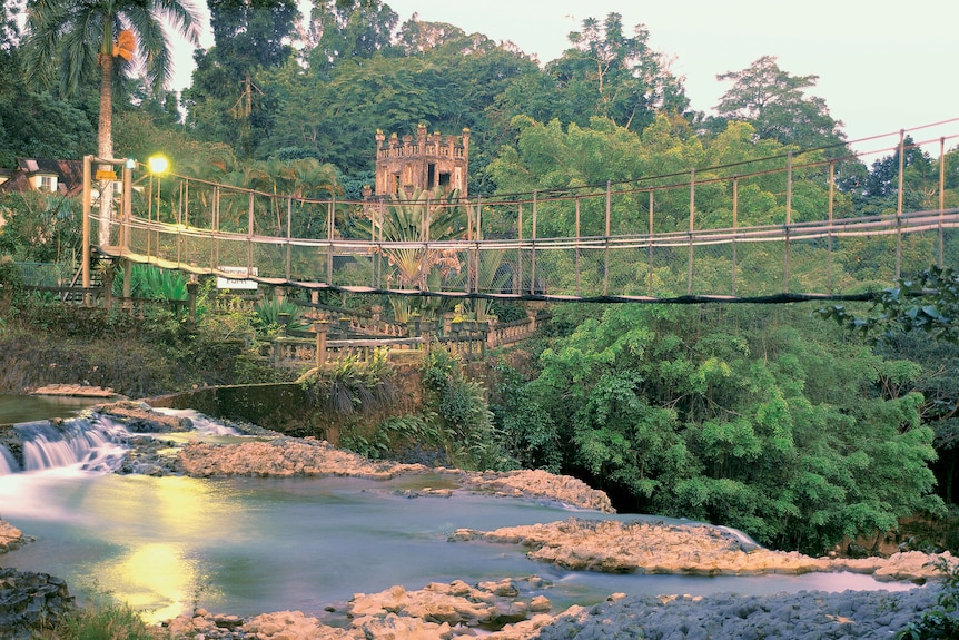a photo of a ropebridge over a waterfall with a castle in the background