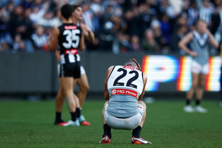 A Port Adelaide player goes down on his haunches with a hand over his face after the final siren.