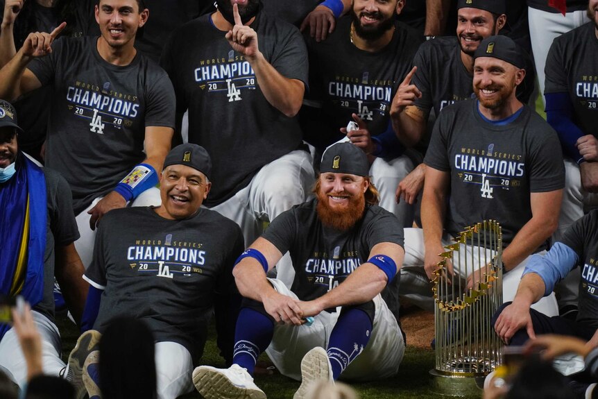 A group of Los Angeles Dodgers players pose with the World Series trophy.