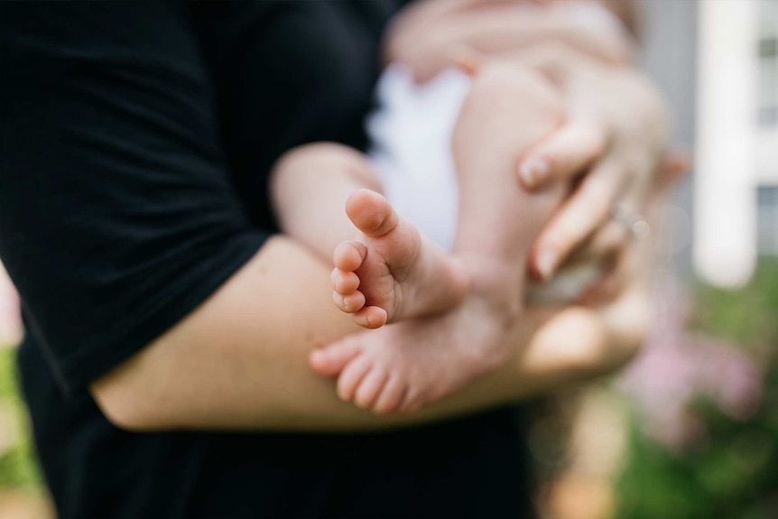 Parent holding a baby with baby feet in focus to depict what to do when you're fired on maternity leave.