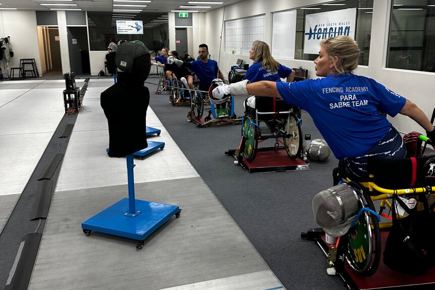 A woman in a wheelchair is practicing fencing with a mannequin. 