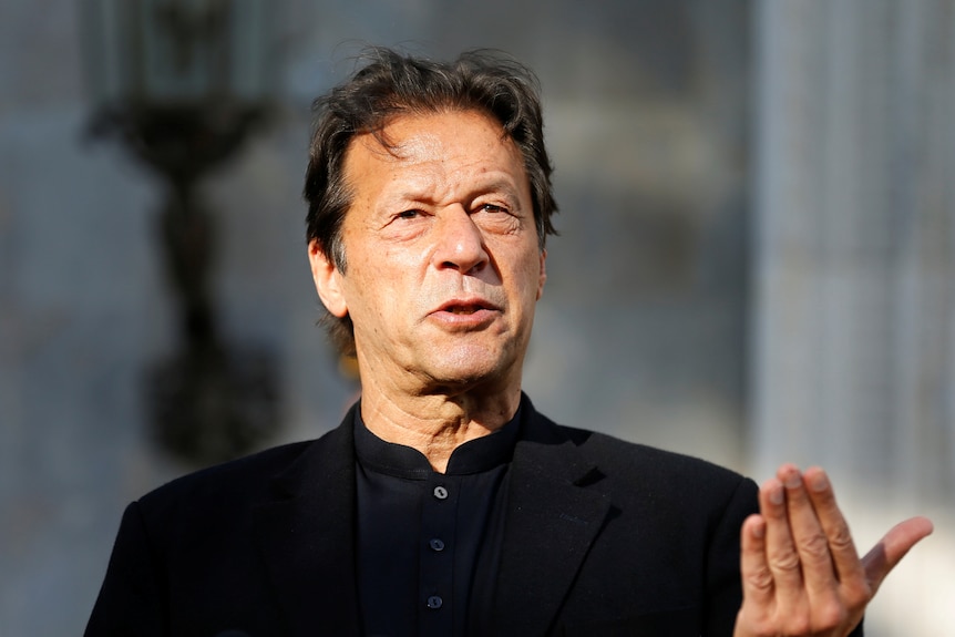A close up of Imran Khan in a black suit as he talks and gestures with his hand.