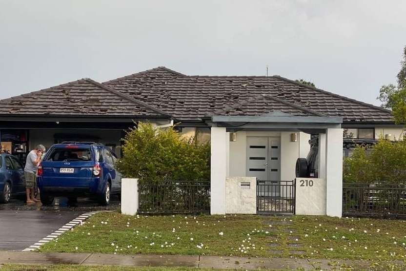 Holes in a roof on a suburban home and hail on the grass. Car windows smashed.