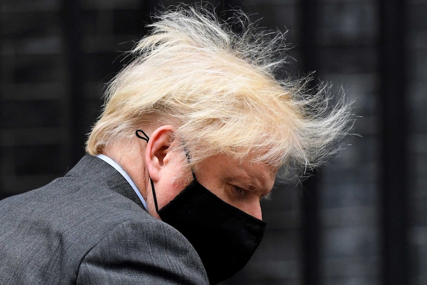 Johnson, wearing a black face mask and wild hair, looks down