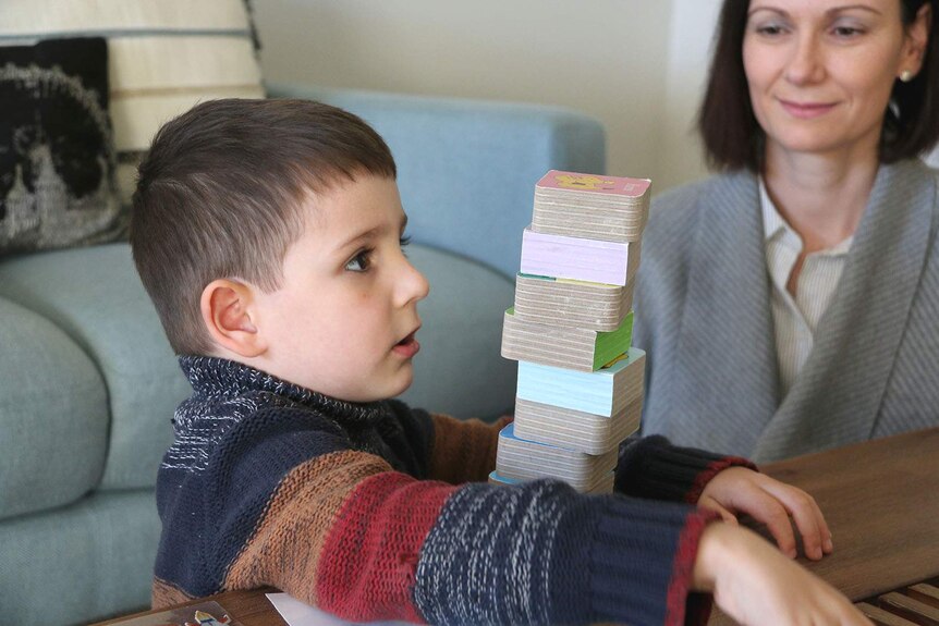 A boy playing with a stack of blocks watched by his mother
