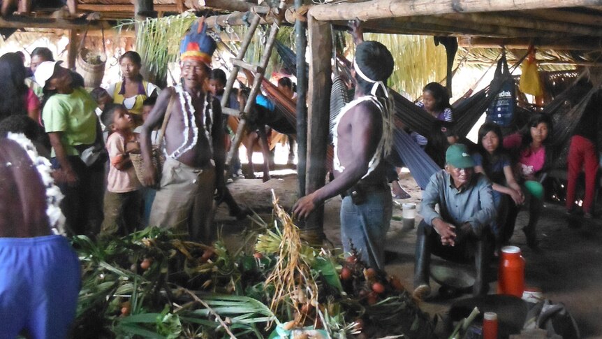 A group of Murui people stand around a pile of food inside inside a traditional roundhouse during festivities.
