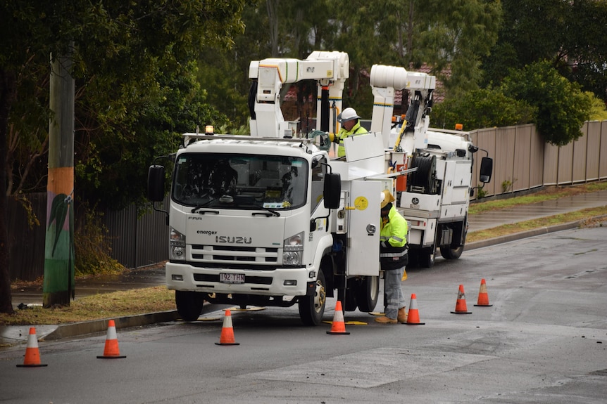 Two energex workers stand near their truck parked by the power pole.