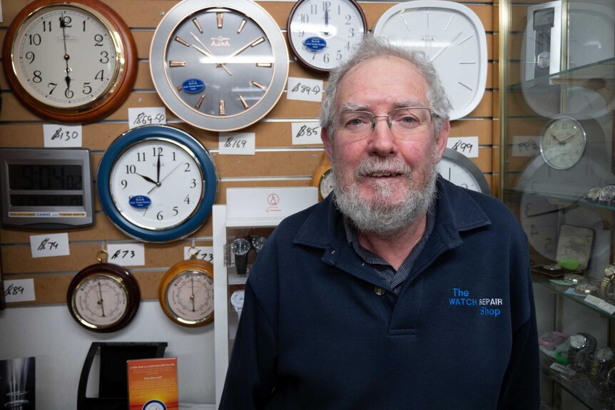 Picture of a man standing in front of a wall of clocks