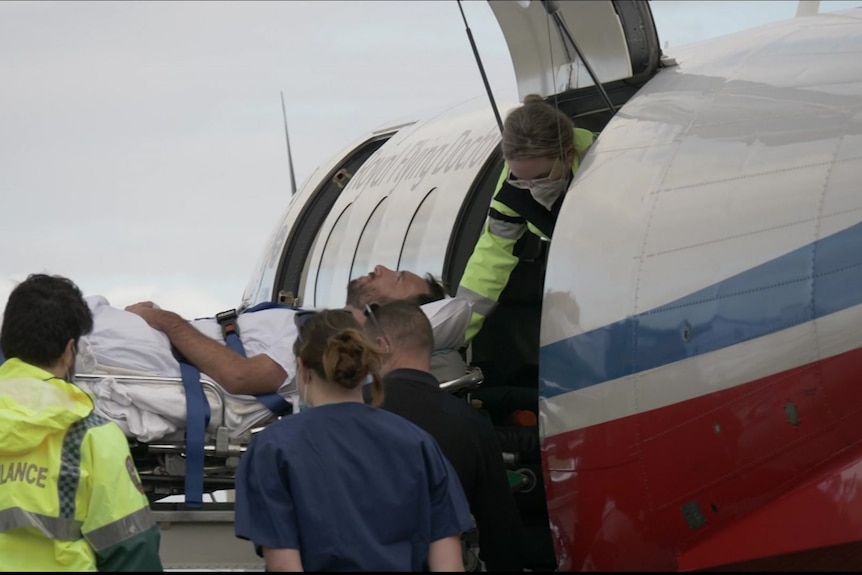 A man is loaded into a plane on a stretcher.