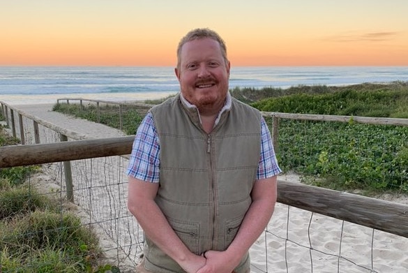 David Newberry stands on a sandy walkway leading to a sunset beach on the Gold Coast.