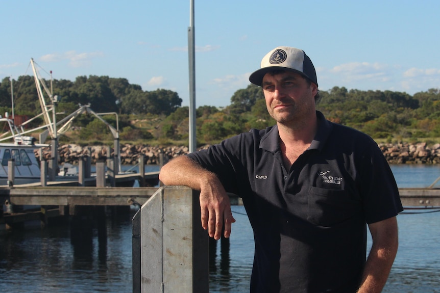 A man stands at a small marine, resting his hand on a post, looking concerned