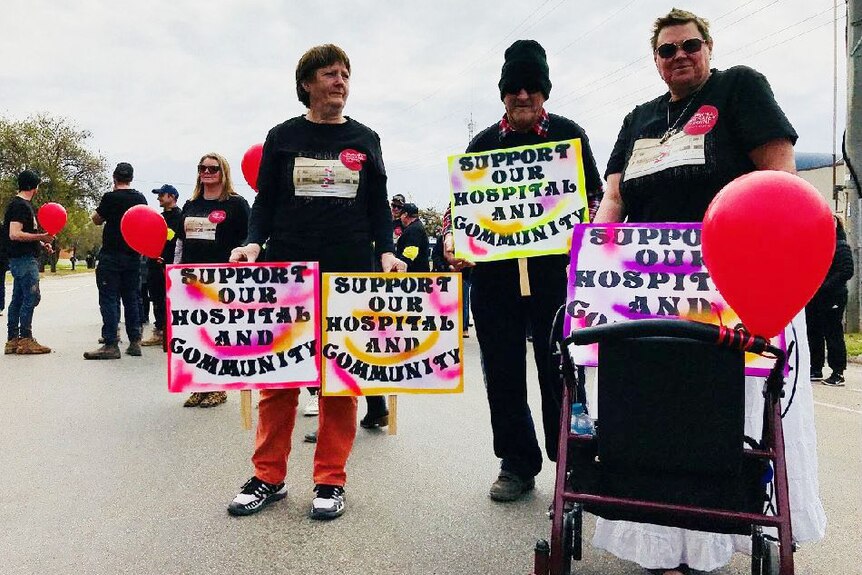 Three people holding signs saying "Support our hospital and community"