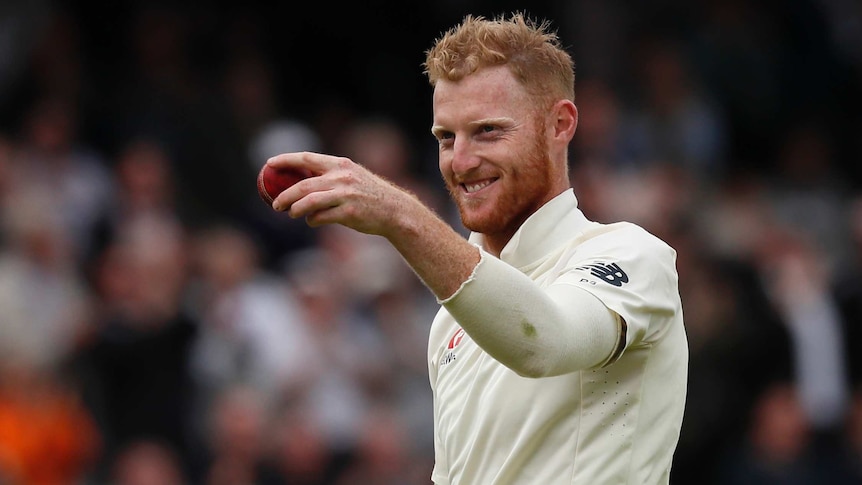 England all rounder Ben Stokes holds a cricket ball to the camera with a grin.