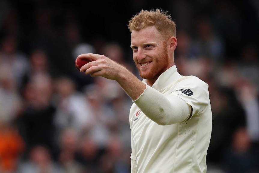 England all rounder Ben Stokes holds a cricket ball to the camera with a grin.