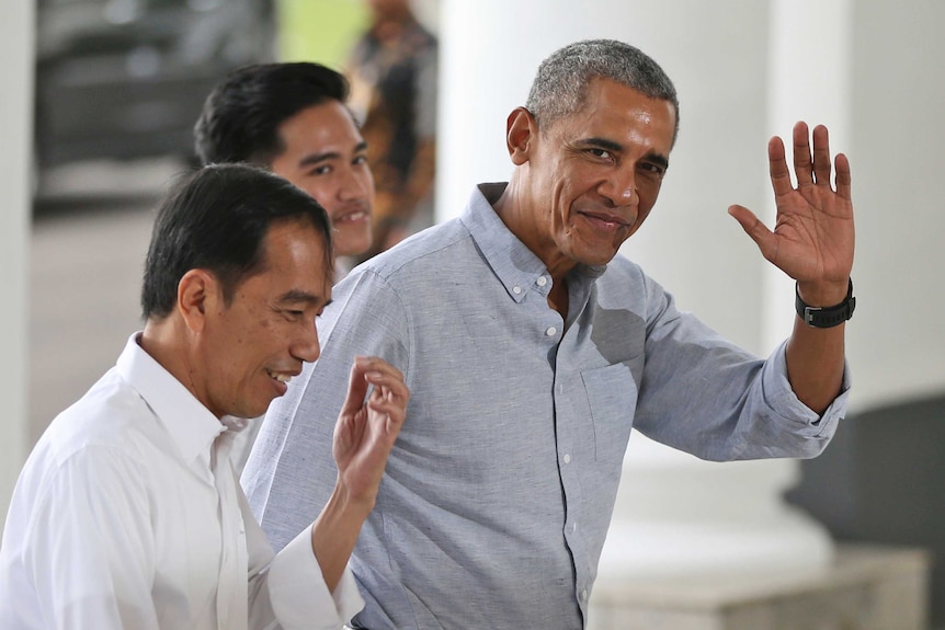 Barack Obama waves with his right hand as he walks and talks with Joko Widodo in the halls of the palace