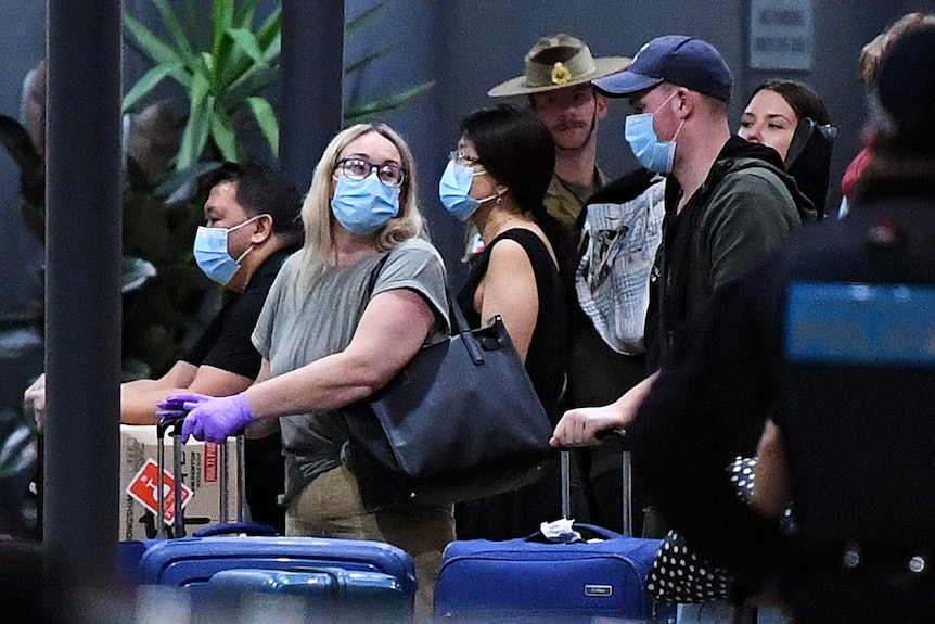Returning overseas traveller wearing face masks talk and hold their bags.