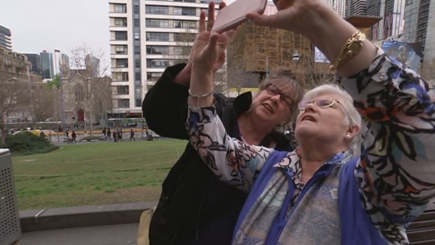 Two women standing outside look up into a smart phone to take a selfie.