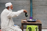 An old man pouring tea into his cup sitting at a table.