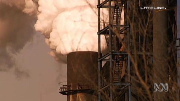 A huge plume of white smoke or steam billows out of a factory chimney