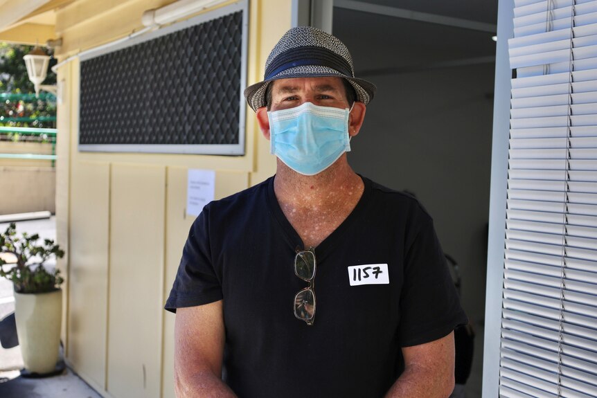 A man wearing a mask and hat standing in front of a building