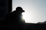 A silhouette of a young man outside with a cap on