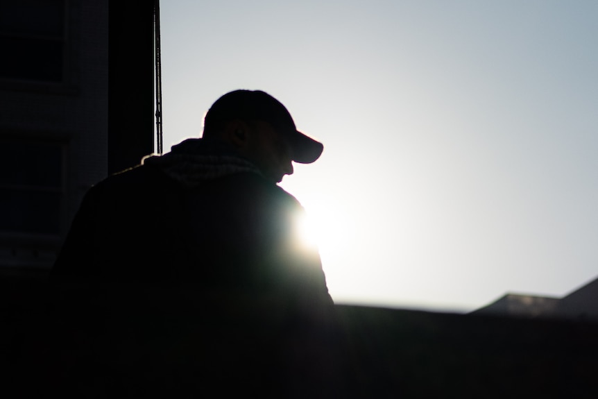 A silhouette of a young man outside with a cap on
