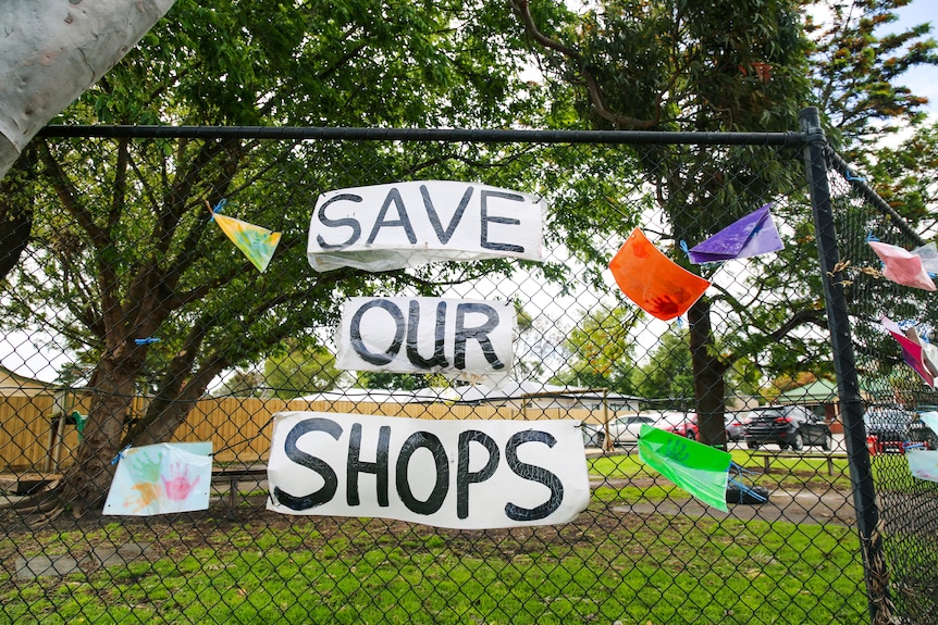 A sign that reads 'save our shops' attached to a chainlink fence