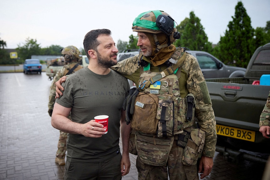 Ukraine's President Volodymyr Zelenskyy speaks to a Ukrainian service member dressed in army gear.