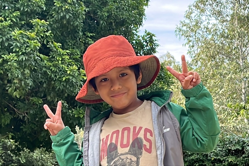 a little boy in an orange bucket hat giving the peace sign