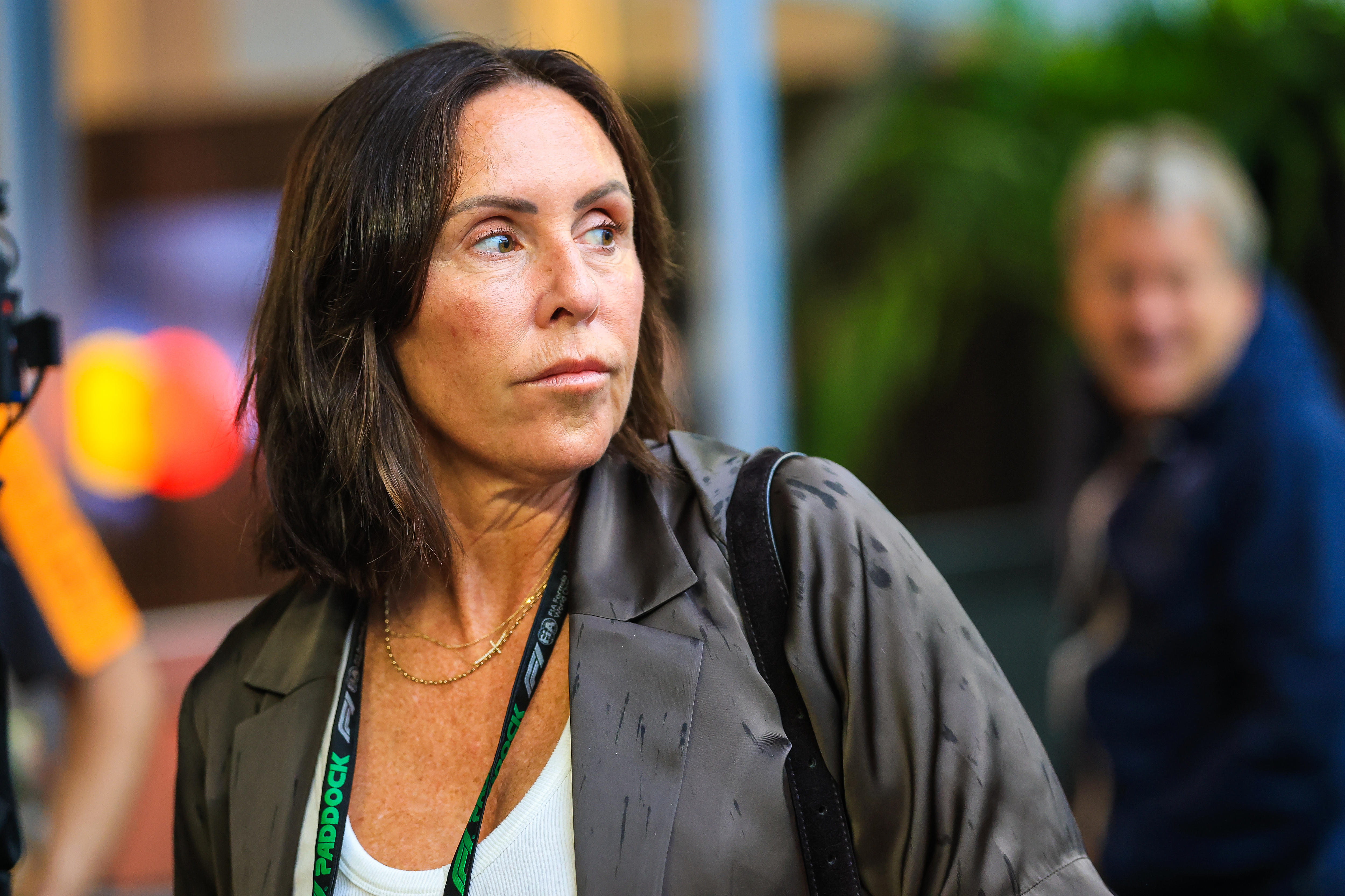 A woman wearing a lanyard stands looking away from the camera at a Formula 1 grand prix weekend.