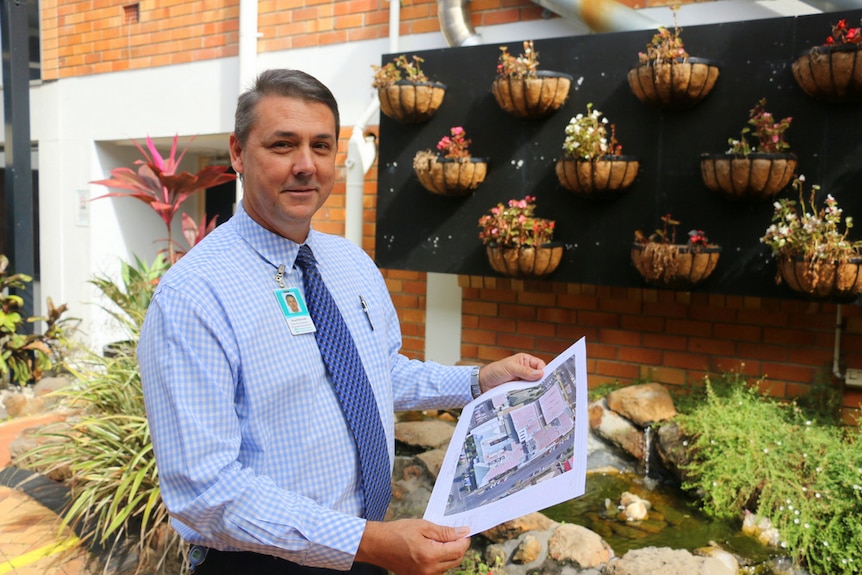 A man wearing a blue and white checked shirt stands holding a plan showing a solar installation project.