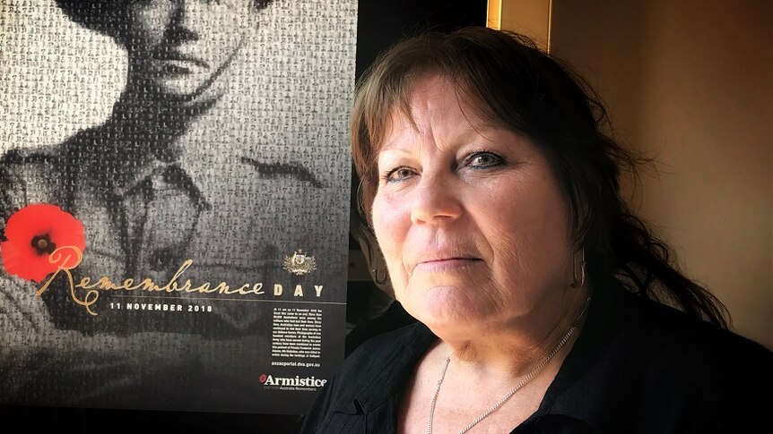 A woman in a black shirt standing in front of a Remembrance Day poster.