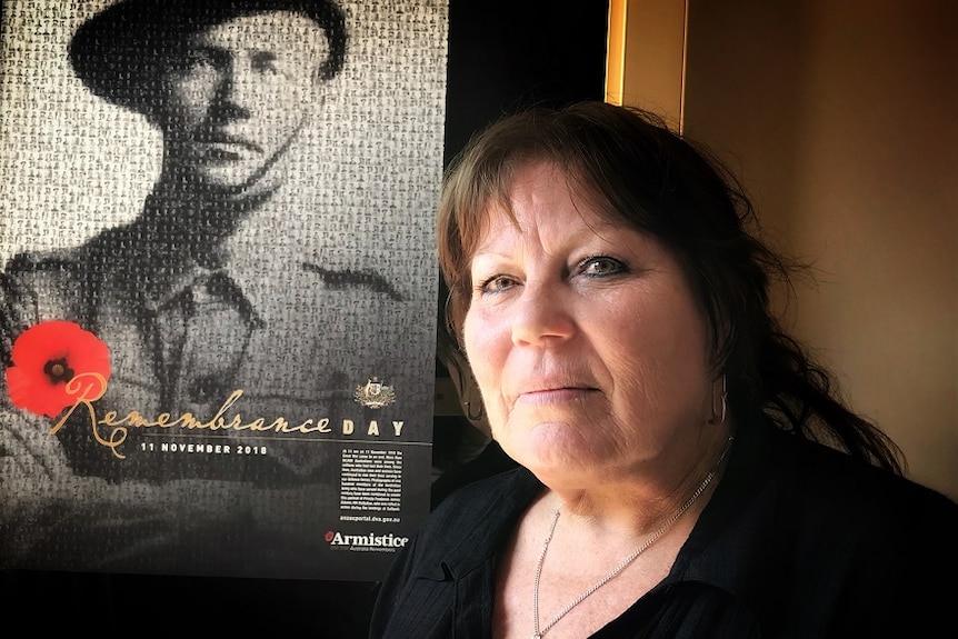 A woman in a black shirt standing in front of a Remembrance Day poster.