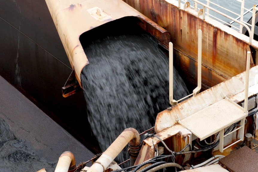 A pipe spews sludge and silt into the hopper of a ship.