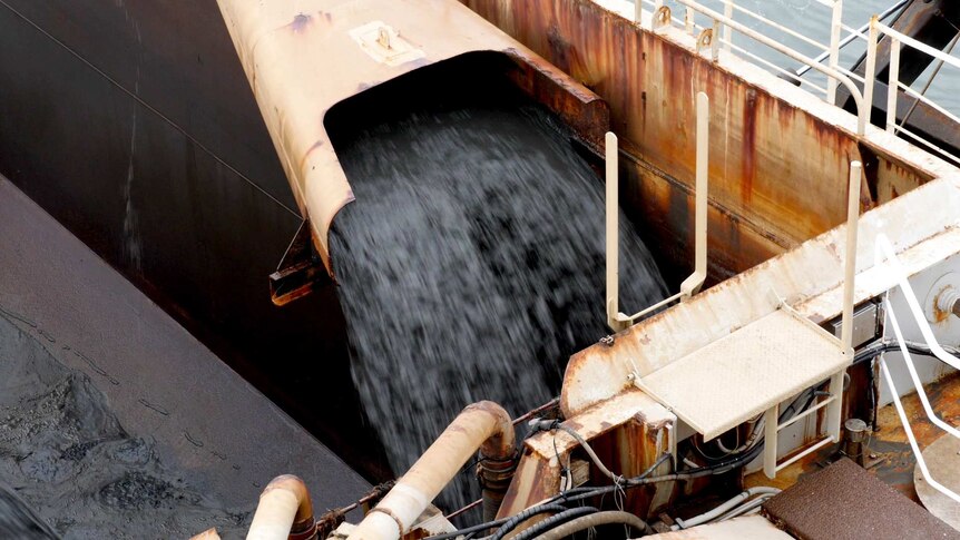 A pipe spews sludge and silt into the hopper of a ship.