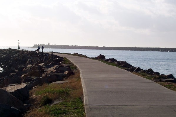 A footpath along a rocky breakwall fringing a harbour.