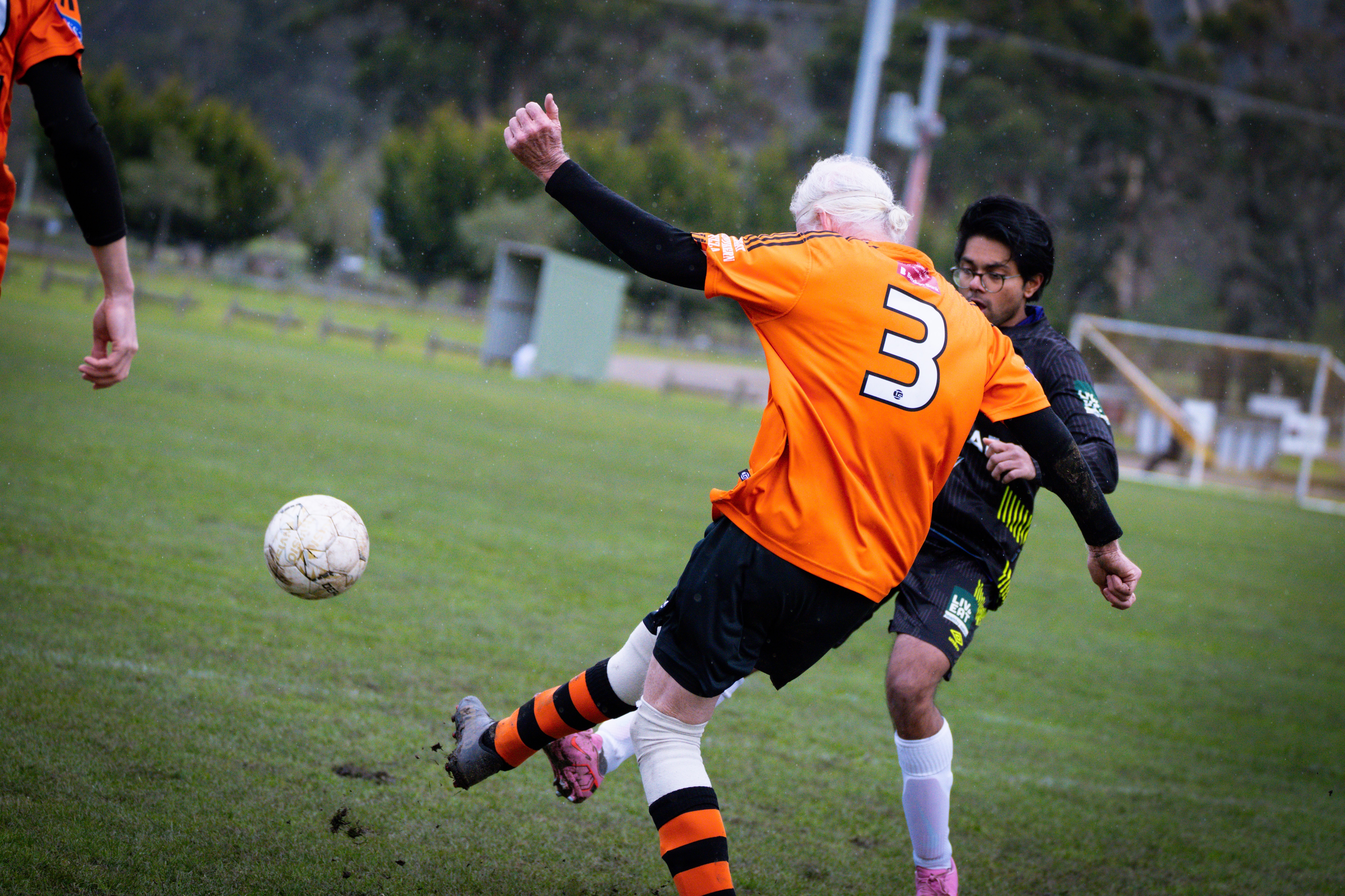 A man with white hair and a long white beard wearing orange soccer colours on a soccer field.