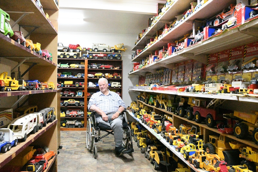 A man in a wheelchair sits surrounded by toy trucks.