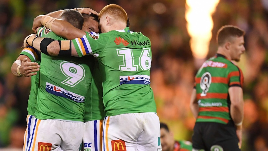 Four NRL players hug each other as they celebrate during a rugby league match.