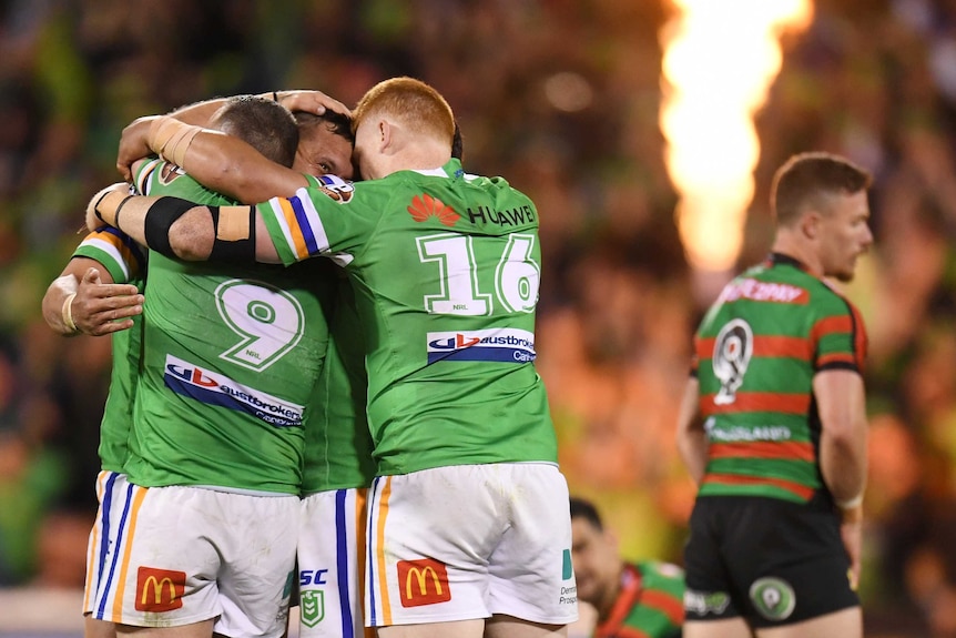 Four NRL players hug each other as they celebrate during a rugby league match.