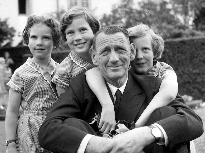 A black-and-white photograph shows a middle-aged wrinkled man smiling with three young girls