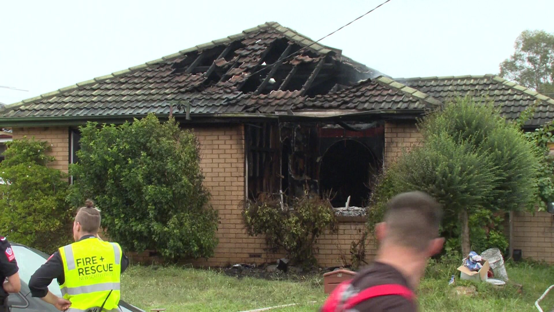 A home with burnt roof and front window as emergency services standing in front 