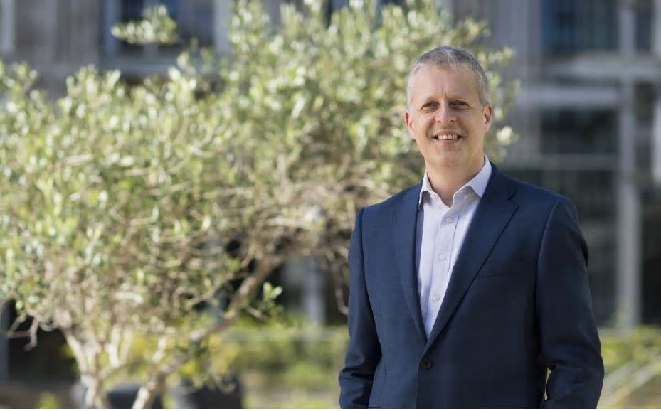 A middle aged man white man with grey hair standing in front of a tree