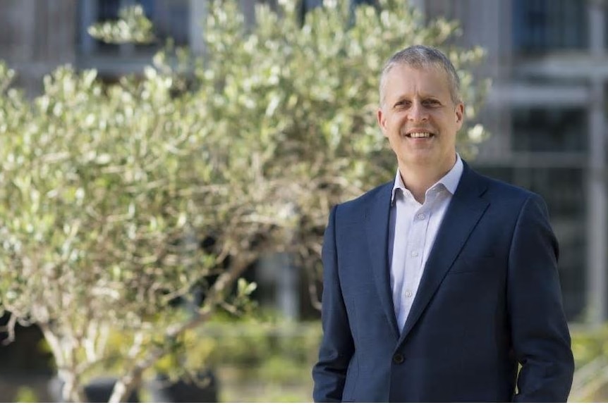 A middle aged man white man with grey hair standing in front of a tree