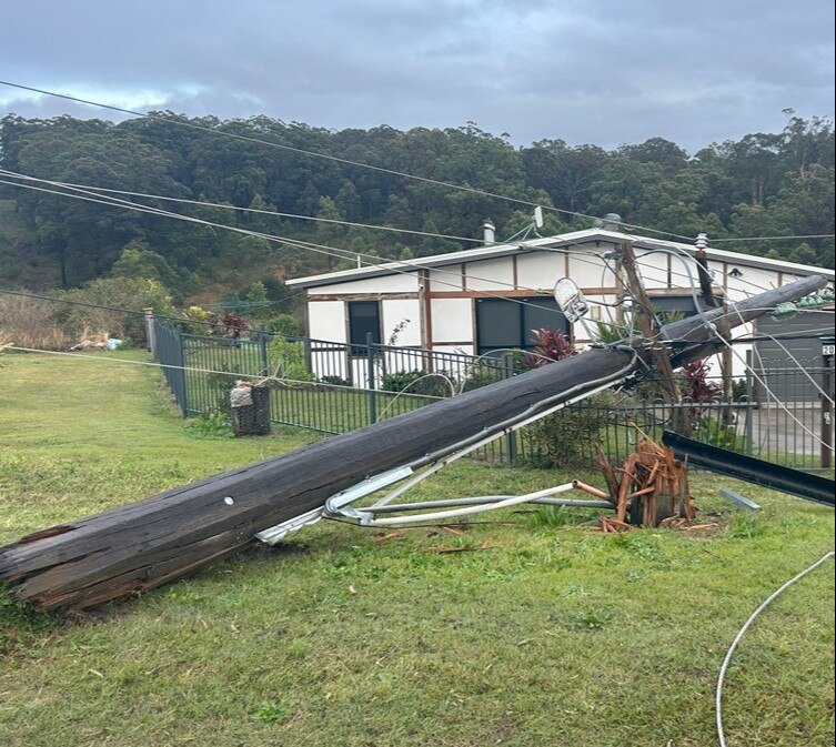 power pole down across white house surrounded by green fields.