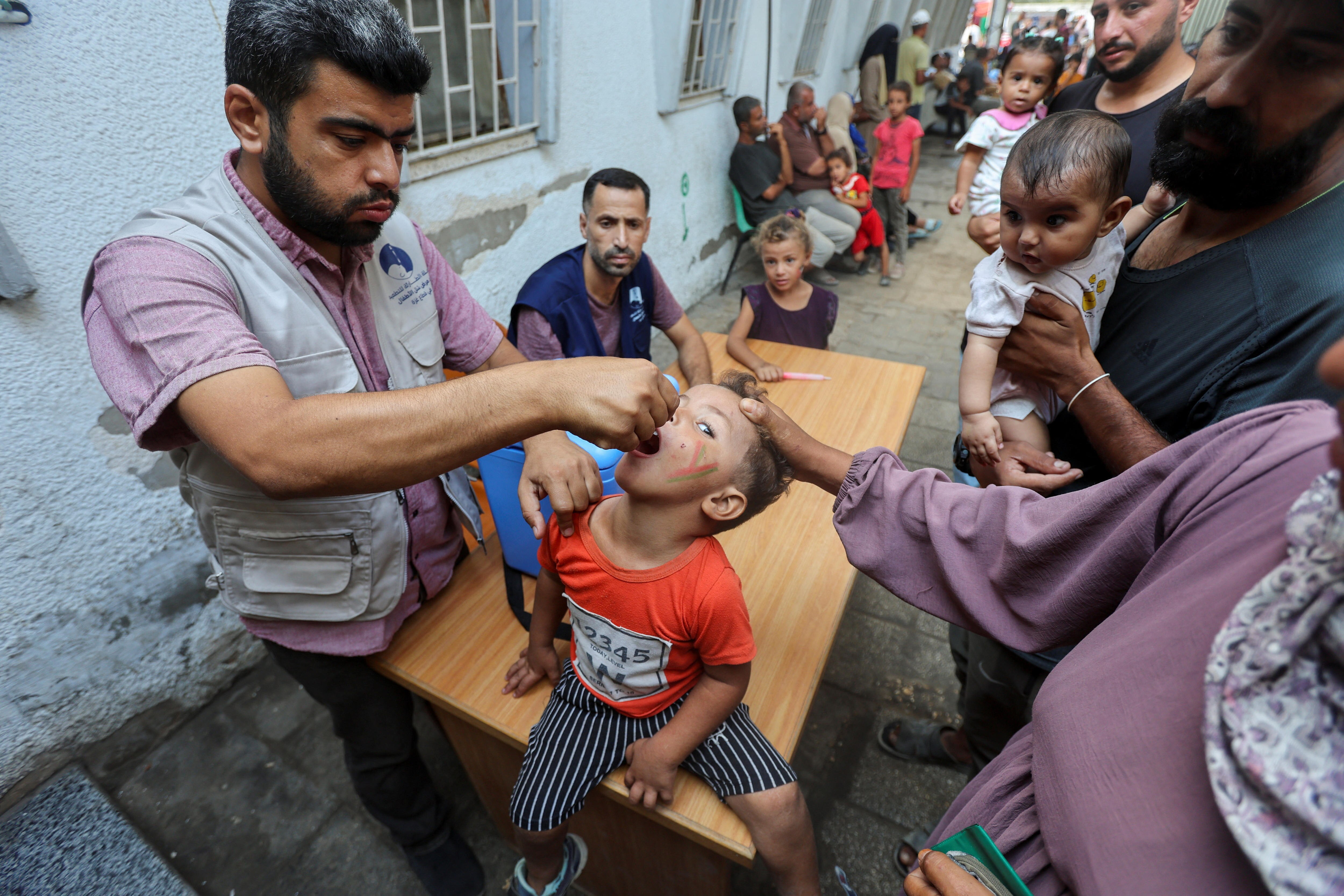 A medic holds a dropper to a child's mouth as people look on in the street