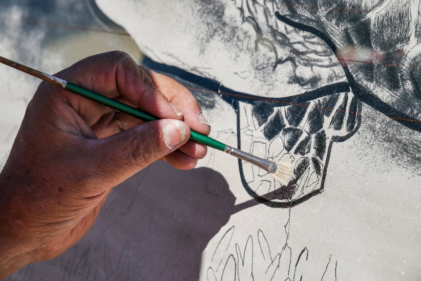 Artist Scott Wade painting the flipper of a turtle in dirt on a car window.