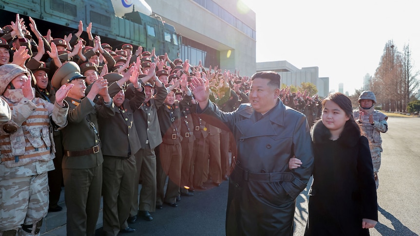 Kim Jung Un waves to a group of people clapping at him next to his daughter