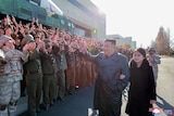 Kim Jung Un waves to a group of people clapping at him next to his daughter